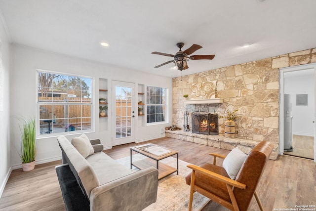 living room featuring baseboards, water heater, a fireplace, wood finished floors, and a ceiling fan