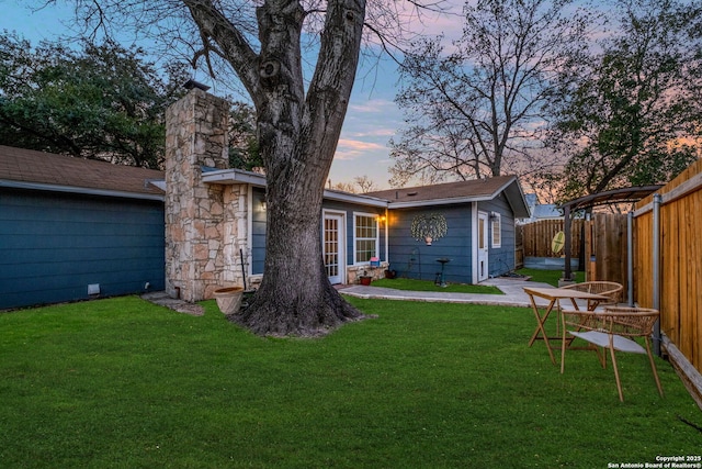 back of property at dusk with a lawn and fence