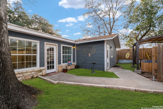 rear view of house with stone siding, a lawn, and fence