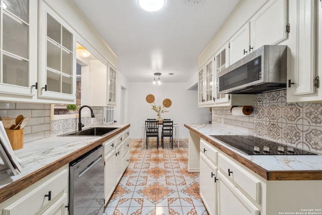 kitchen with light tile patterned floors, a sink, decorative backsplash, stainless steel appliances, and white cabinets