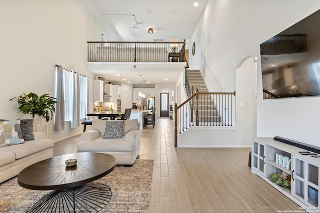 living room featuring light wood-style flooring, recessed lighting, a high ceiling, baseboards, and stairs