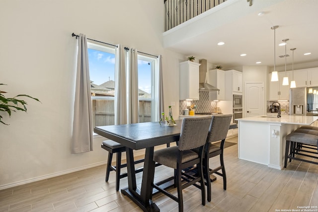 dining room with wood finish floors, baseboards, a high ceiling, and recessed lighting