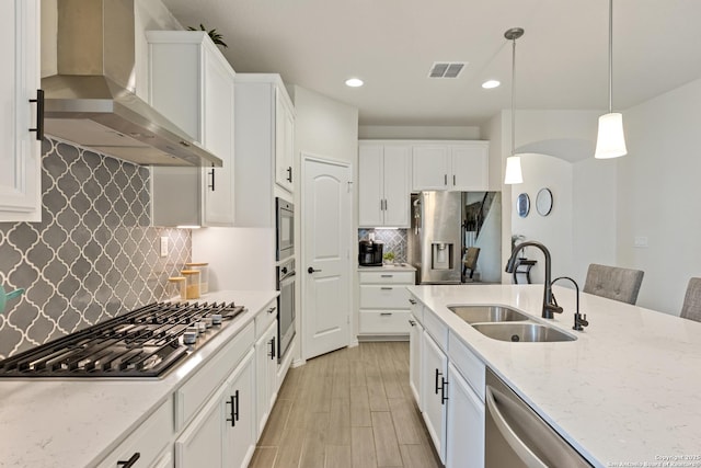 kitchen featuring visible vents, a sink, white cabinetry, appliances with stainless steel finishes, and wall chimney exhaust hood