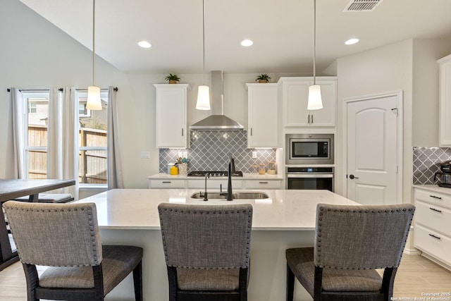 kitchen with appliances with stainless steel finishes, a breakfast bar, wall chimney range hood, and a sink