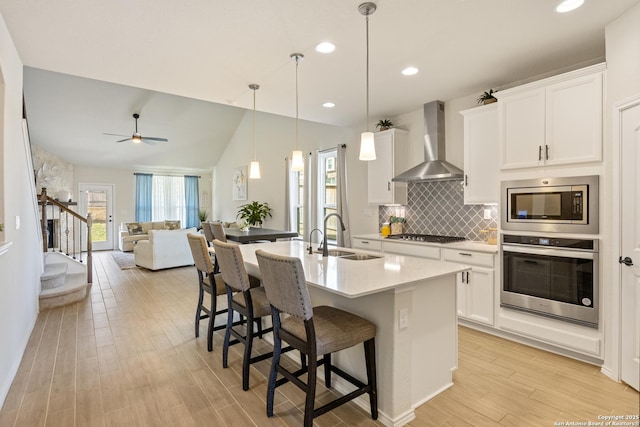 kitchen with light wood-style flooring, a sink, stainless steel appliances, a breakfast bar area, and wall chimney exhaust hood