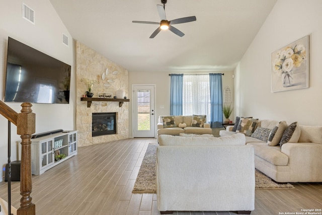 living area featuring visible vents, wood finish floors, lofted ceiling, a stone fireplace, and a ceiling fan