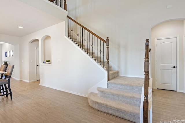 staircase with baseboards, wood tiled floor, recessed lighting, arched walkways, and a towering ceiling