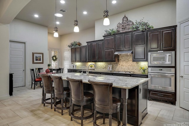 kitchen featuring a sink, a towering ceiling, backsplash, and stainless steel appliances