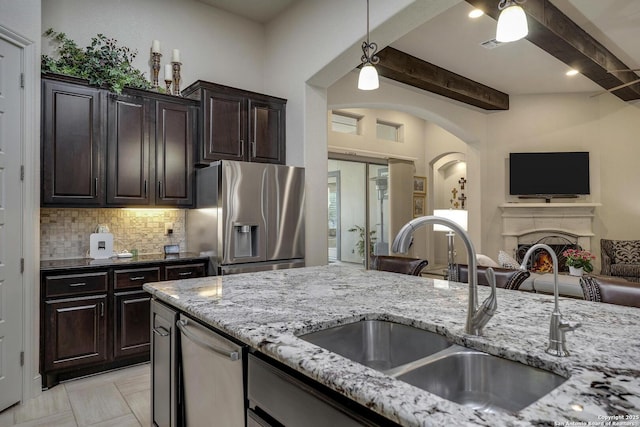 kitchen with backsplash, light stone counters, appliances with stainless steel finishes, a warm lit fireplace, and a sink