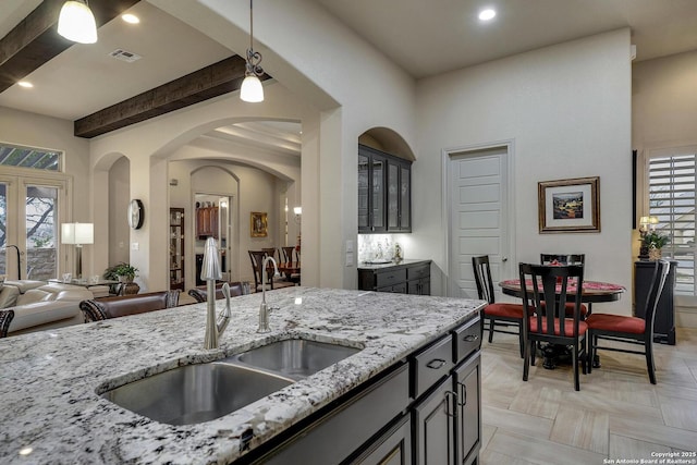 kitchen with light stone countertops, visible vents, beam ceiling, a sink, and decorative light fixtures