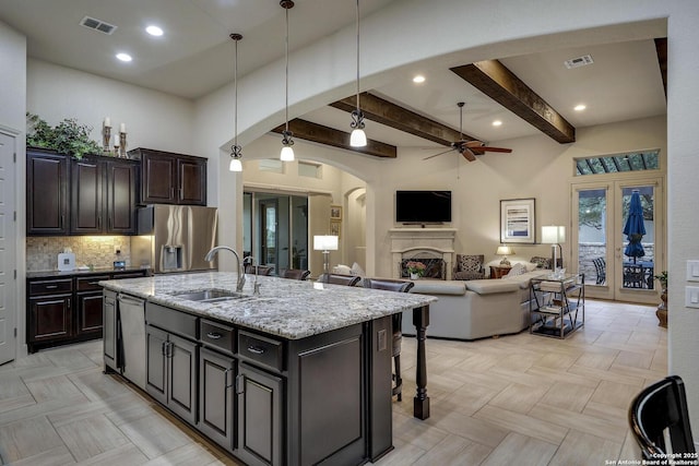 kitchen featuring visible vents, a fireplace, arched walkways, stainless steel appliances, and a sink