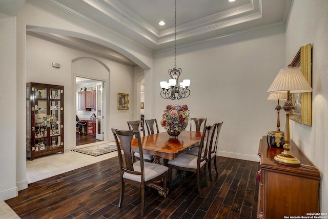 dining space with a tray ceiling, crown molding, arched walkways, and wood finish floors