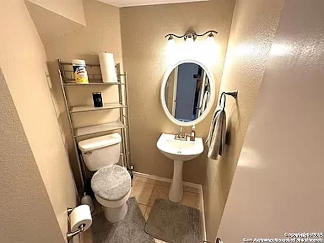 bathroom featuring toilet, baseboards, and a textured wall