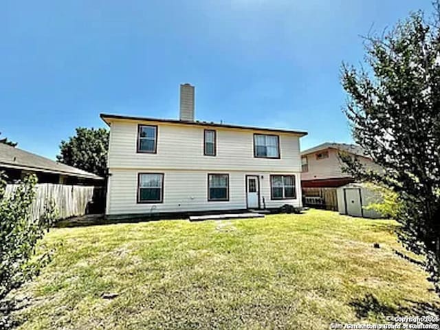 back of house with a fenced backyard, a chimney, an outdoor structure, a storage unit, and a lawn