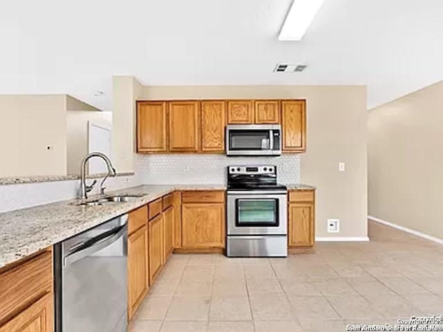 kitchen featuring a sink, backsplash, stainless steel appliances, light tile patterned flooring, and light stone countertops