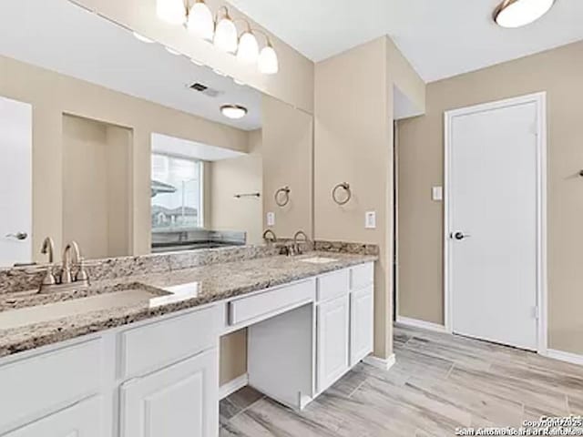 bathroom with double vanity, wood finished floors, baseboards, and a sink