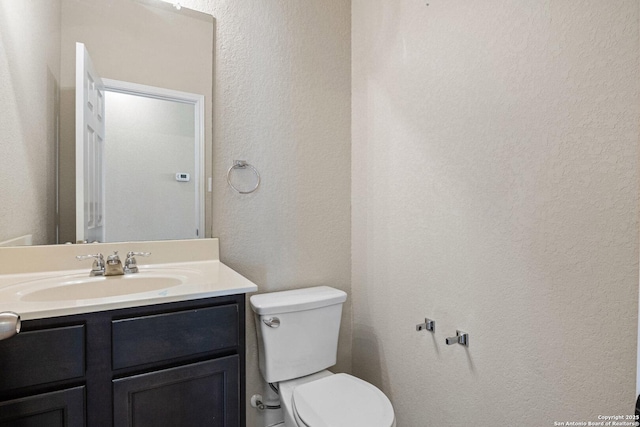 half bath featuring toilet, vanity, and a textured wall