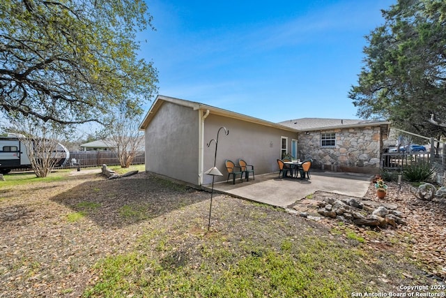 back of property featuring a patio area, stone siding, stucco siding, and fence