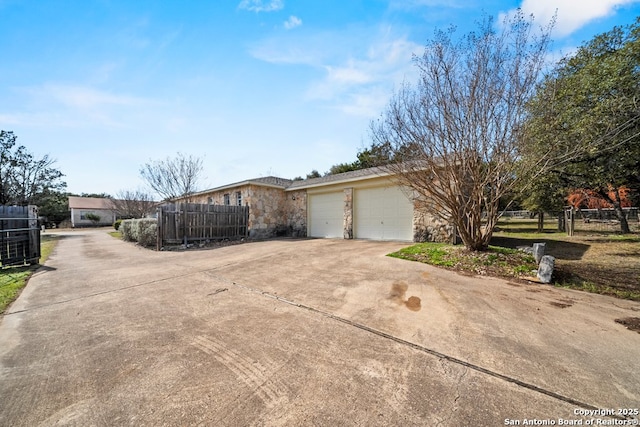 view of property exterior featuring central air condition unit, driveway, stone siding, fence, and a garage