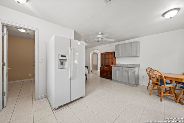 kitchen featuring ceiling fan, light tile patterned floors, gray cabinets, white fridge with ice dispenser, and arched walkways