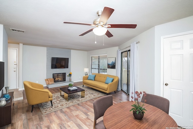 living room with visible vents, baseboards, a fireplace, wood finished floors, and a ceiling fan