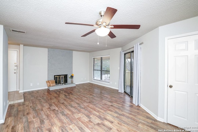 unfurnished living room with a brick fireplace, wood finished floors, visible vents, and a textured ceiling