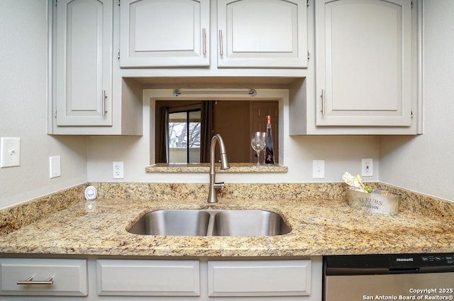 kitchen featuring a sink, light stone counters, stainless steel dishwasher, and white cabinetry