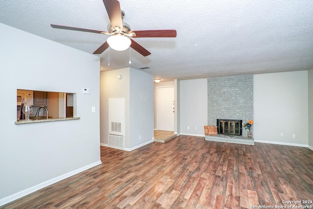 unfurnished living room featuring wood finished floors, baseboards, visible vents, a textured ceiling, and a brick fireplace