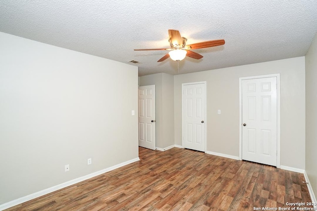 unfurnished bedroom featuring a ceiling fan, visible vents, wood finished floors, baseboards, and a textured ceiling