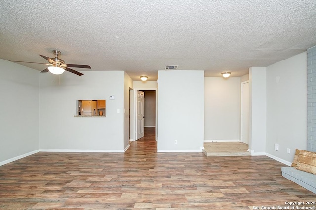 empty room with a ceiling fan, wood finished floors, visible vents, baseboards, and a textured ceiling