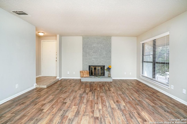 unfurnished living room featuring visible vents, a fireplace, a textured ceiling, and wood finished floors