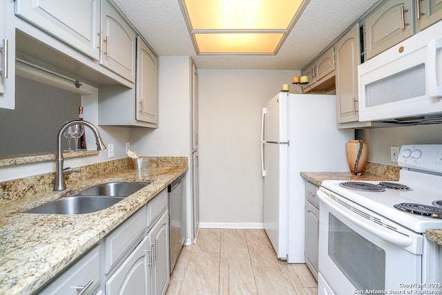 kitchen featuring white appliances, light stone counters, baseboards, a sink, and a textured ceiling