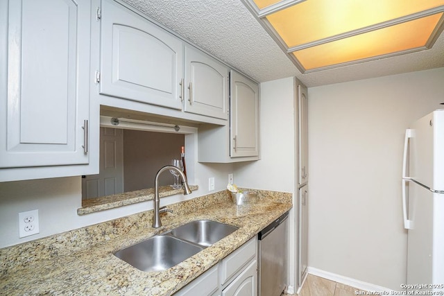 kitchen featuring light stone countertops, stainless steel dishwasher, freestanding refrigerator, a textured ceiling, and a sink