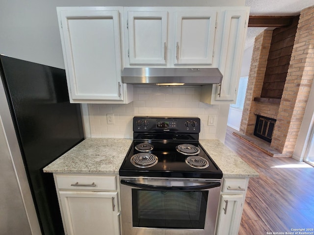 kitchen featuring freestanding refrigerator, white cabinets, under cabinet range hood, and range with electric stovetop