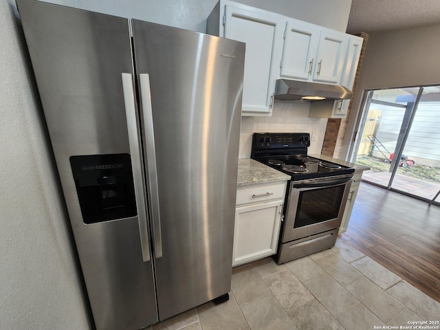 kitchen featuring under cabinet range hood, backsplash, stainless steel appliances, white cabinets, and light stone countertops