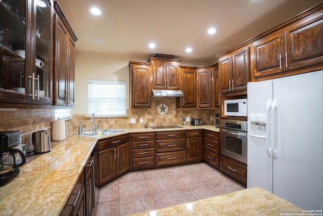 kitchen with tasteful backsplash, under cabinet range hood, recessed lighting, white appliances, and a sink