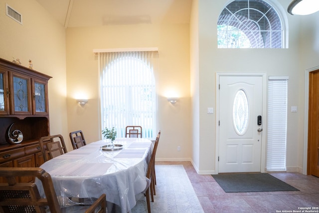 dining space with tile patterned floors, visible vents, baseboards, and a towering ceiling