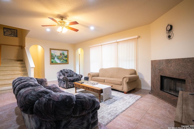 living area with a ceiling fan, light tile patterned flooring, arched walkways, a high end fireplace, and stairs