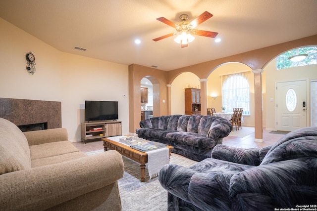 living room featuring a ceiling fan, visible vents, light tile patterned flooring, a fireplace, and arched walkways