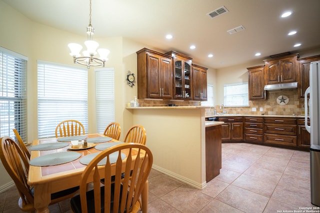 kitchen with visible vents, under cabinet range hood, a sink, backsplash, and light tile patterned floors