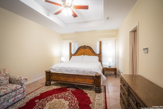 bedroom featuring visible vents, baseboards, a tray ceiling, light tile patterned floors, and a ceiling fan