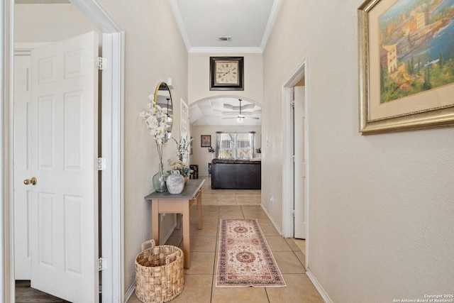 hall featuring baseboards, visible vents, arched walkways, crown molding, and tile patterned floors