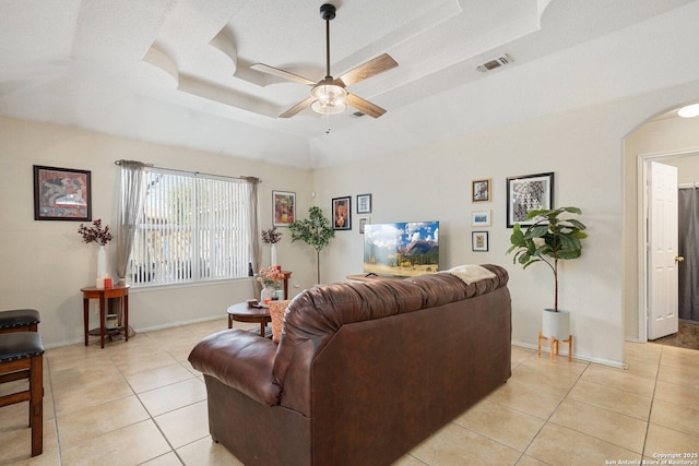 living room with arched walkways, visible vents, a raised ceiling, and a ceiling fan