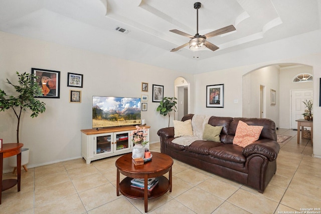 living area with visible vents, ceiling fan, a tray ceiling, light tile patterned floors, and arched walkways