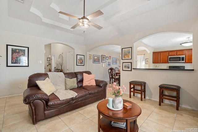 living room featuring arched walkways, light tile patterned floors, a raised ceiling, and a ceiling fan