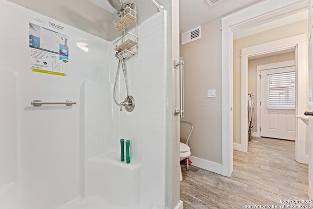 bathroom featuring baseboards, wood finished floors, visible vents, and a stall shower