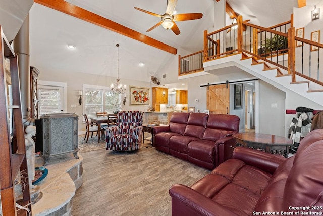 living room featuring beam ceiling, ceiling fan with notable chandelier, wood finished floors, a barn door, and stairs