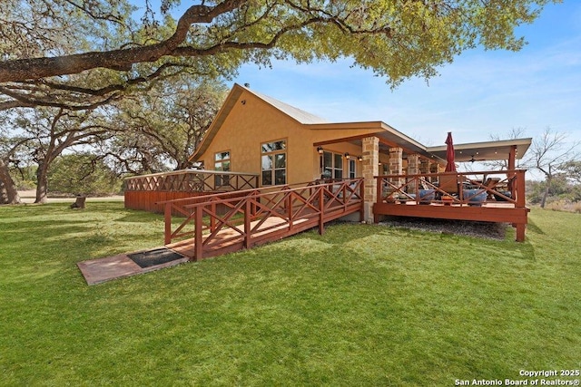 rear view of property featuring a wooden deck, a yard, stone siding, and stucco siding