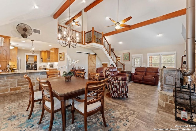 dining area featuring beamed ceiling, washer and dryer, wood finished floors, a barn door, and a wood stove