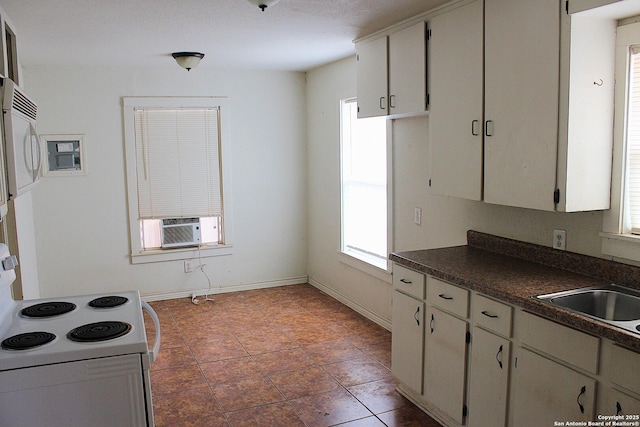 kitchen featuring dark countertops, baseboards, cooling unit, white appliances, and a sink